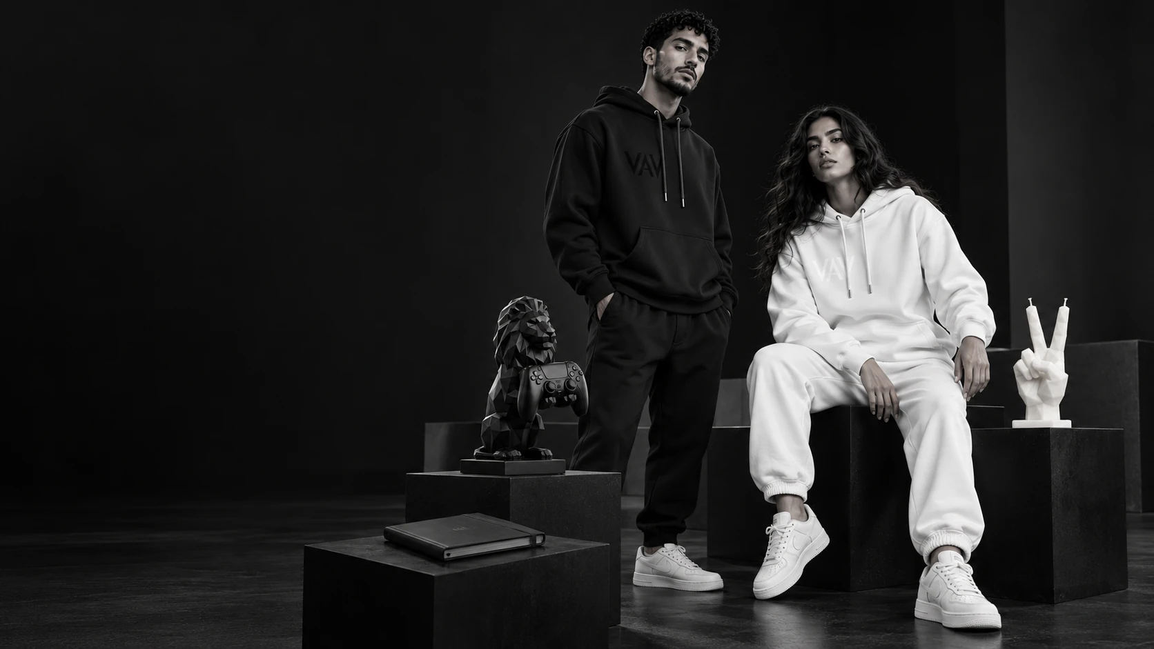 Two models in black and white VAV streetwear, with the Atlas Lion holder, V Sign candle and notebook displayed on plinths.